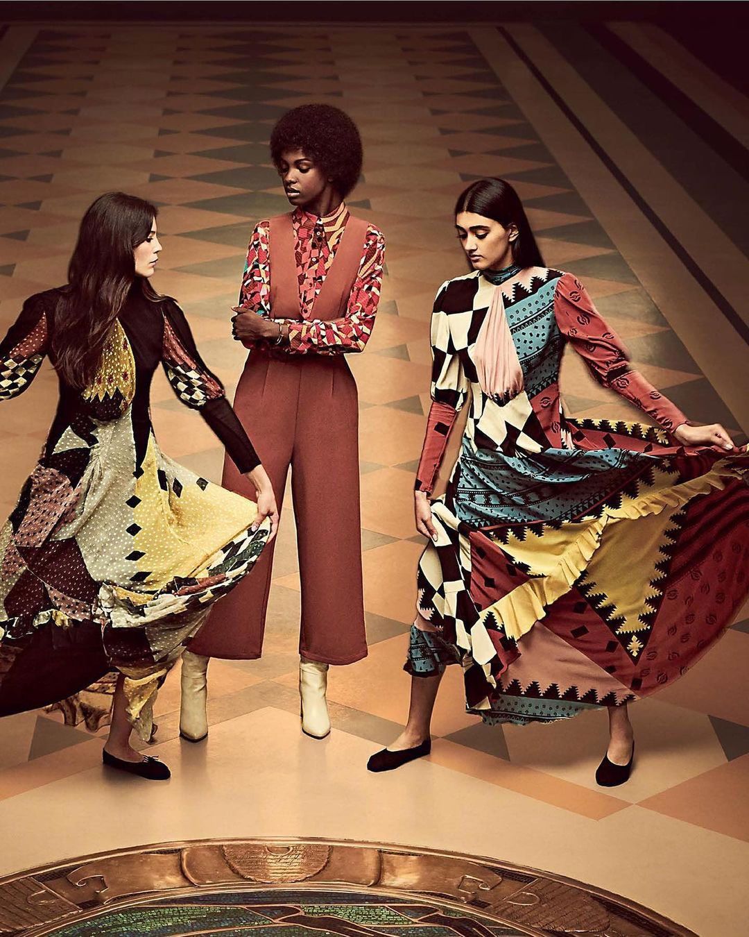 Three women showcase patterned dresses and elegant fashion in a studio shot with a vintage-inspired set design and warm, inviting lighting.