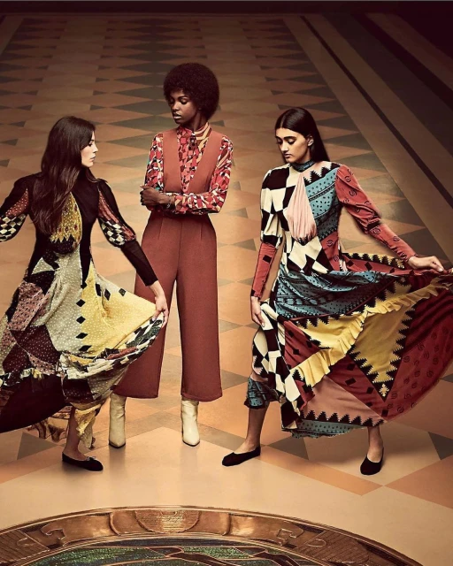 Three women showcase patterned dresses and elegant fashion in a studio shot with a vintage-inspired set design and warm, inviting lighting.