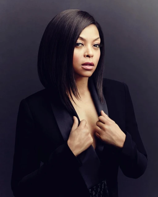 Glamour shot of an African American woman in a black blazer with sleek black hair against a dark grey backdrop in a studio.