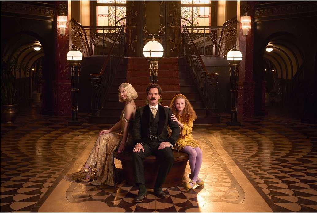 Elegant family portrait in a grand lobby featuring a man, woman, and child, with ornate details, warm lighting, and period costumes.