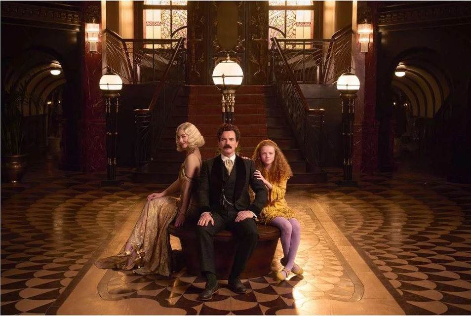 Elegant family portrait in a grand lobby featuring a man, woman, and child, with ornate details, warm lighting, and period costumes.