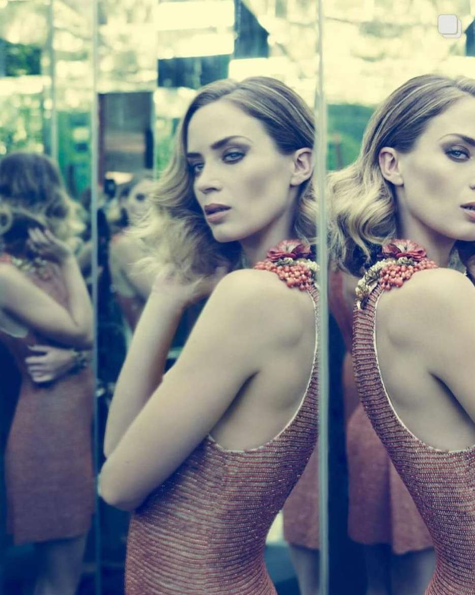 Portrait of a woman wearing a dress with decorative shoulder embellishments and posing in front of a mirror wall reflecting the scene.