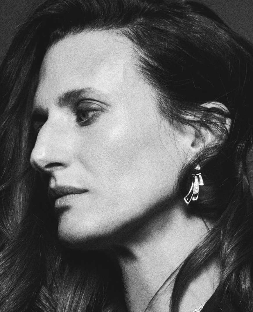 Monochrome portrait of an adult woman with long hair in profile, showcasing an earring and elegant jewelry against a dark backdrop.