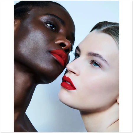 Two adult women of different ethnicities with red lipstick posing closely in a beauty shot with diffused lighting in a photo studio.
