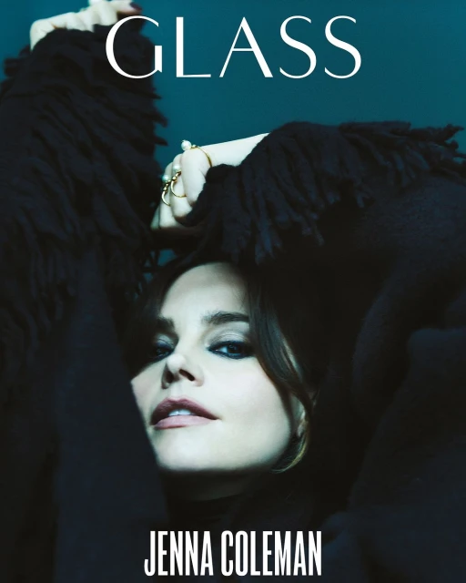 Jenna Coleman portrait on a magazine cover. She wears a black fringed garment and minimal jewelry, posing with her hands near her face.