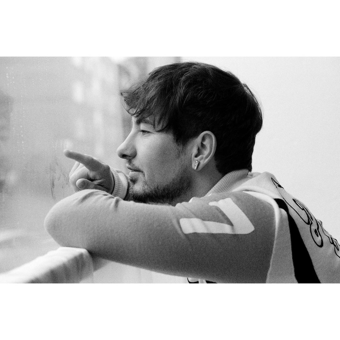 Monochrome portrait of a young adult man looking out a window and pointing, with natural light and soft focus.