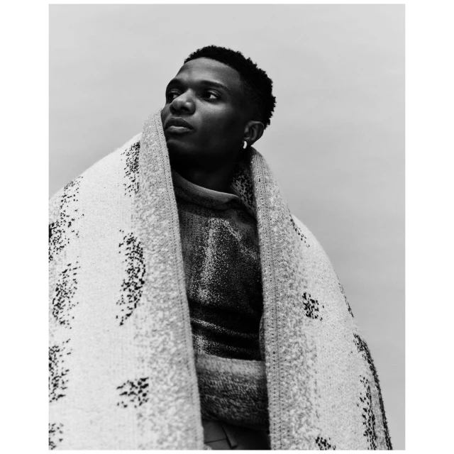 Portrait of an adult male wearing a patterned sweater and a large patterned shawl, looking slightly off-camera to the left.