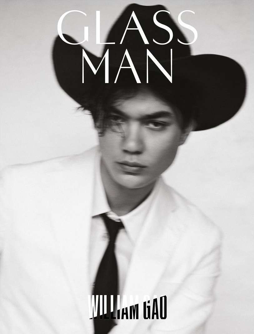 Black and white portrait of a person with a black cowboy hat, white suit jacket, and black tie looking at the camera. 