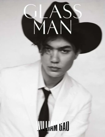 Black and white portrait of a person with a black cowboy hat, white suit jacket, and black tie looking at the camera. 