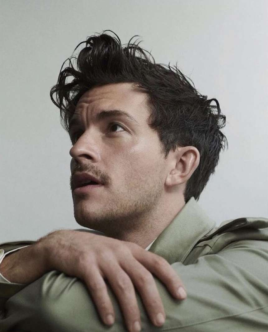 Portrait of a light-skinned adult male with dark hair and a mustache, looking up and away from the camera while resting his arms.