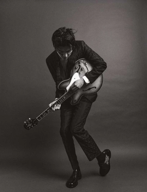 Black and white portrait of an adult male musician playing an electric guitar in a photo studio with dark neutral background.