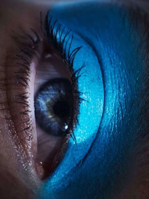 Close-up of a female eye with bright blue eyeshadow on the eyelid and lower lash line and dark eyelashes.
