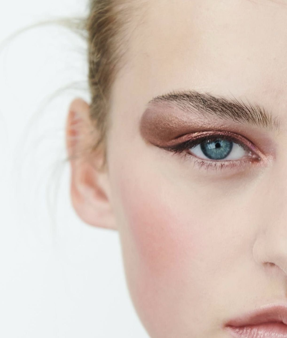 Close-up of woman's face with striking copper eyeshadow and liner against a white background. Beauty and makeup concept.