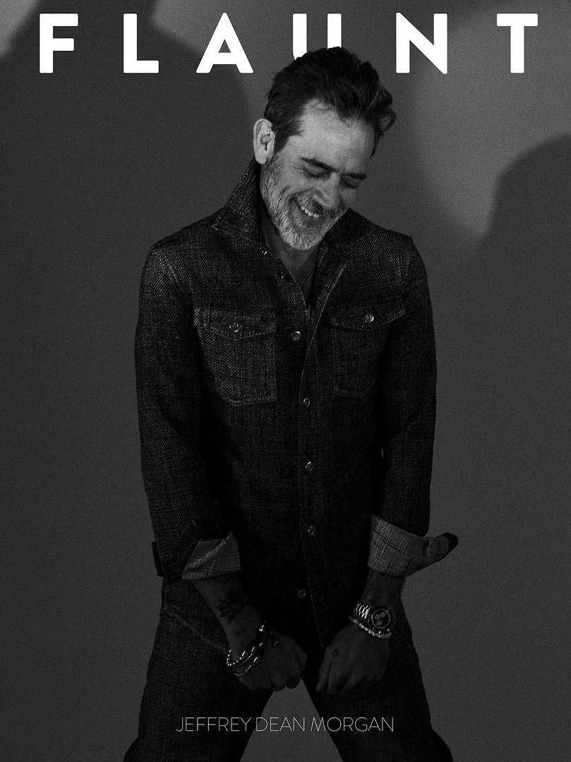 Black and white portrait of Jeffrey Dean Morgan on Flaunt magazine cover, smiling and looking down, wearing a denim shirt and pants.