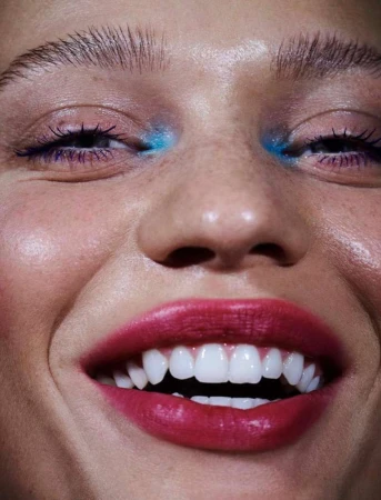 Close-up of a woman's smiling face showcasing vibrant makeup with red lipstick and bright blue eyeshadow, highlighting a beauty aesthetic.