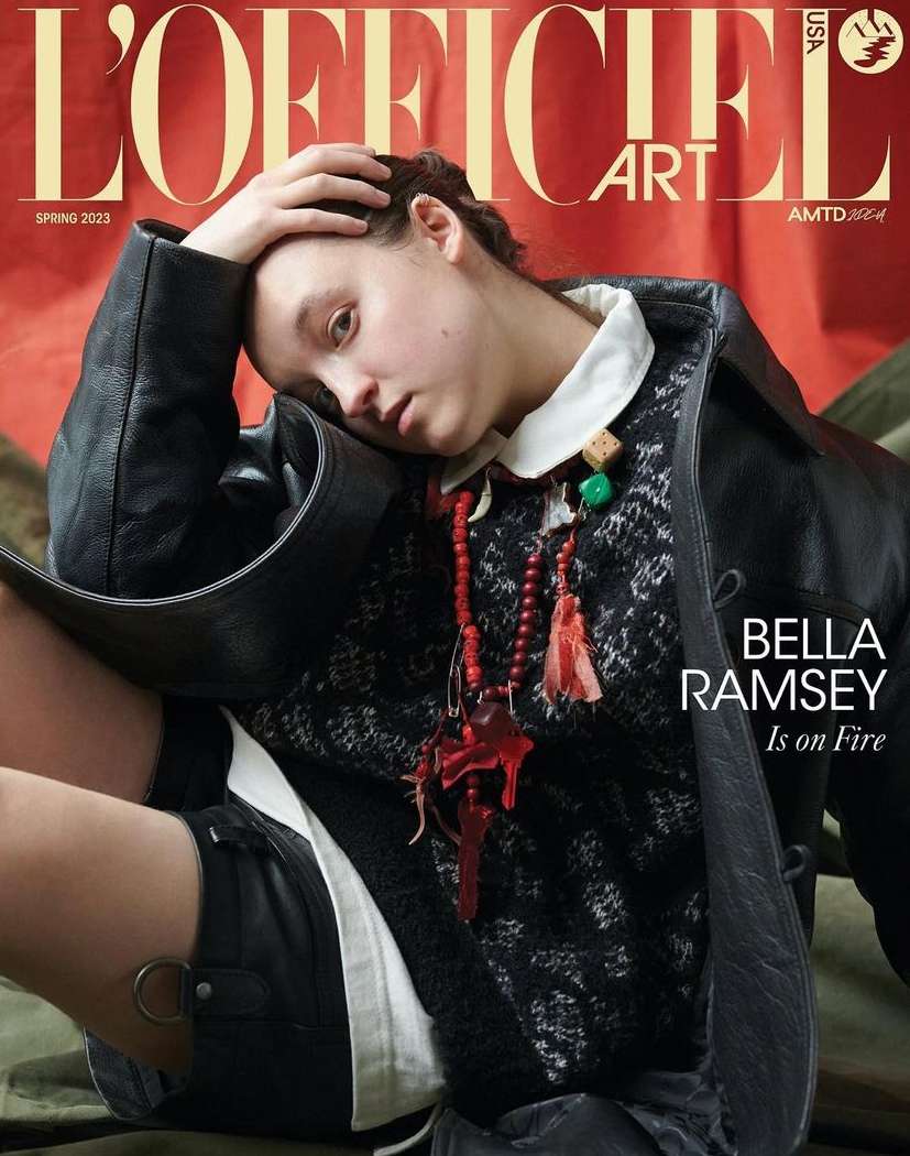 Bella Ramsey on the cover of L'Officiel Art USA Spring 2023. Ramsey wears a black coat and stands out against the red background.