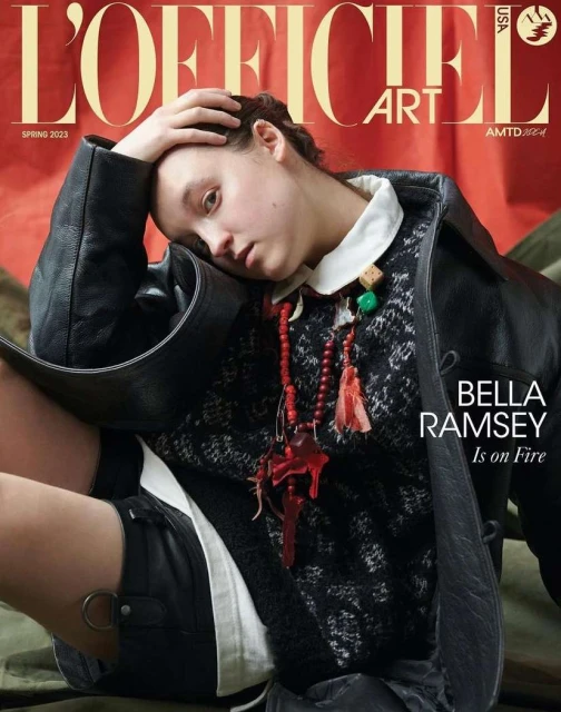 Bella Ramsey on the cover of L'Officiel Art USA Spring 2023. Ramsey wears a black coat and stands out against the red background.
