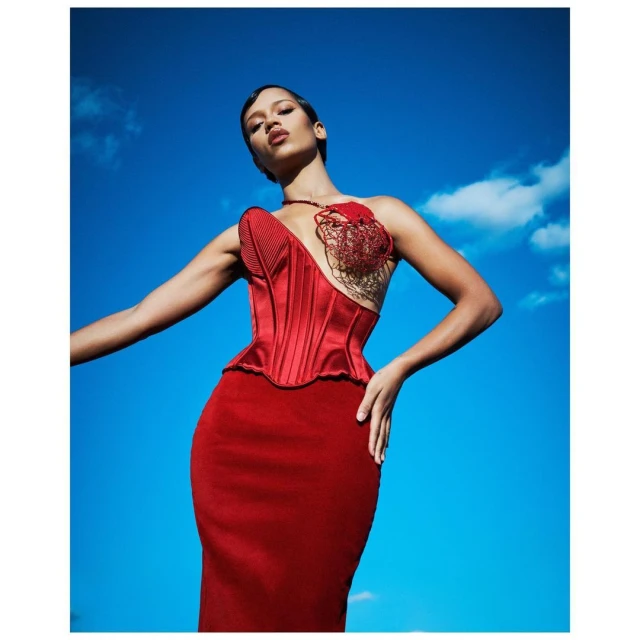 A woman in a red dress poses against a bright blue sky with scattered clouds, highlighting fashion and outdoor photography.