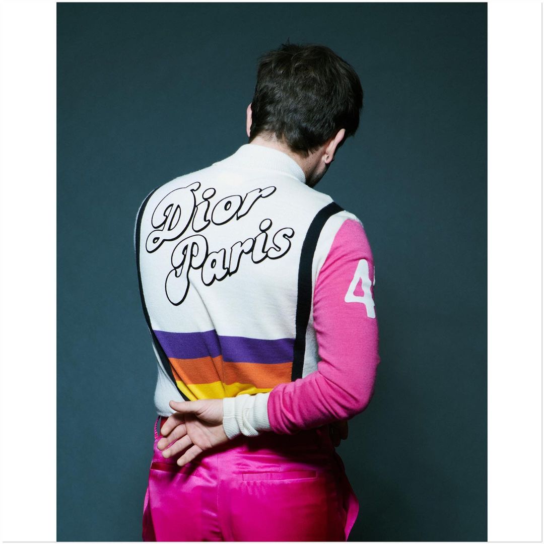 Man with back to camera wearing 'Dior Paris' sweater and bright pink pants in a studio setting, fashion photography, back view.