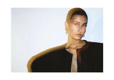 Portrait of a woman wearing a black top and gold earrings against a white background by Jason Hetherington