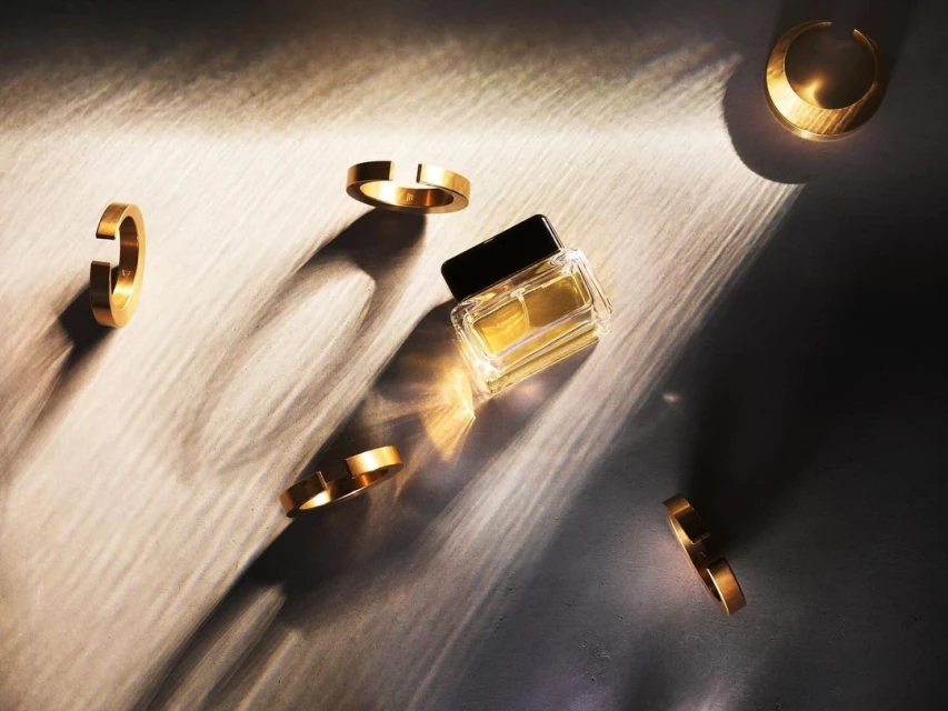 High-angle shot of gold rings and a perfume bottle casting shadows on a surface, creating an elegant and minimalist composition.