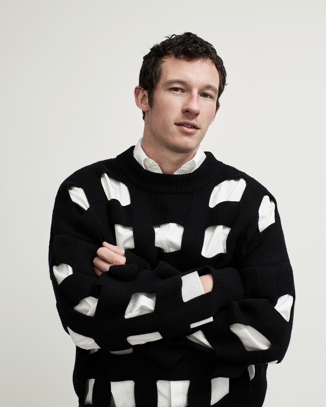 Portrait of an adult male wearing a black sweater with white accents, shot indoors against a plain white backdrop in eye-level view.