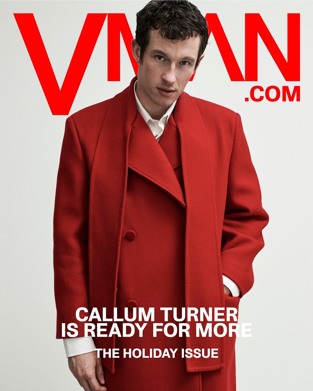 Magazine cover featuring Callum Turner in a red coat, with bold red text "VMAN" and ".COM" on a clean white background. The Holiday Issue.
