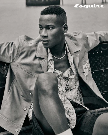 Portrait of a stylish, dark-skinned adult male in an unbuttoned jacket and floral shirt, sitting outdoors. A modern and fashionable look.