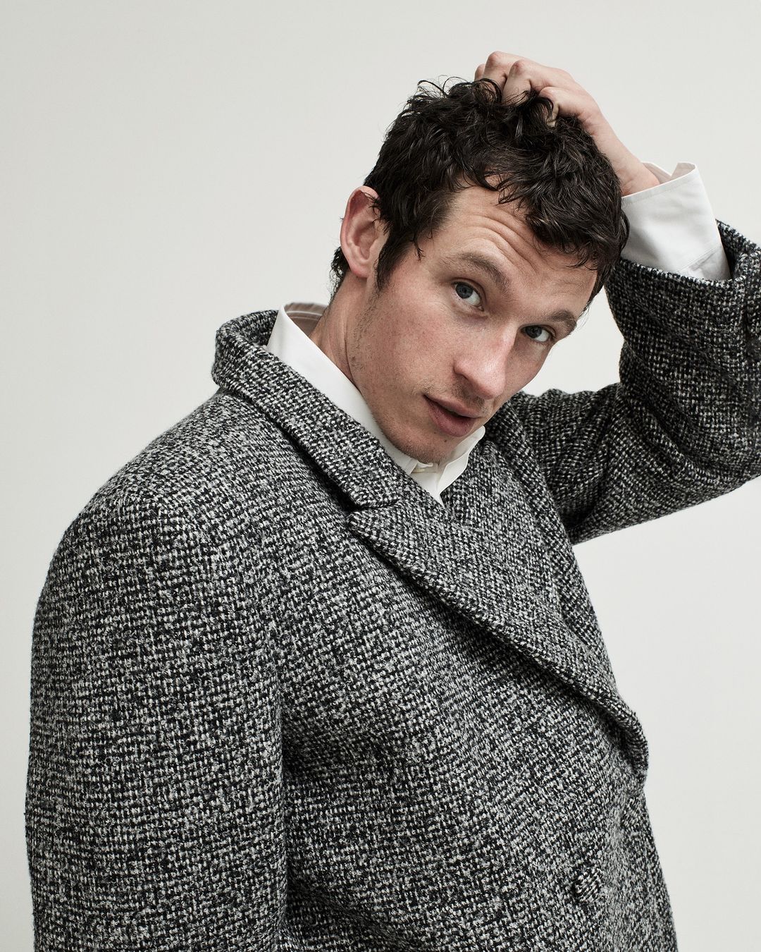 Portrait of a man with dark hair and a tweed coat against a plain background, styled with a classic white shirt collar.