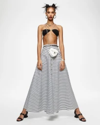 Model with spiky buns wearing a black bandeau top, striped long skirt, and white heart-shaped crossbody bag