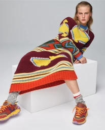 Model in colorful patterned knit dress sitting on a white box wearing patterned sneakers