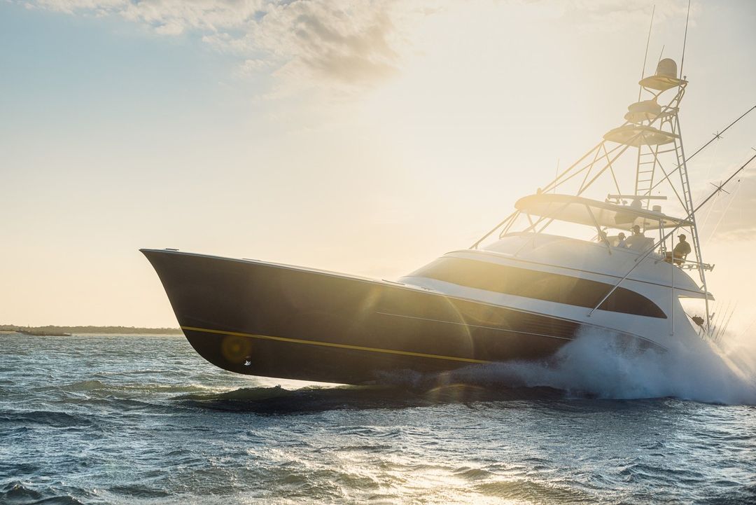 Luxury sport fishing yacht speeding through ocean waters, showcasing a blue and white hull against a backdrop of sunlight and waves.
