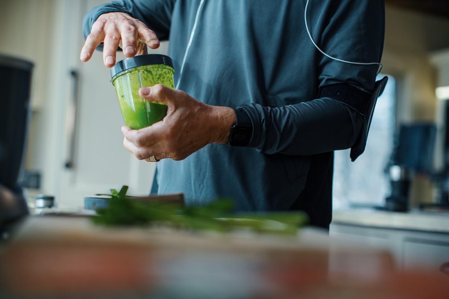 Adult male in athletic wear prepares a green smoothie in a modern kitchen, highlighting a healthy lifestyle with a focus on nutrition.