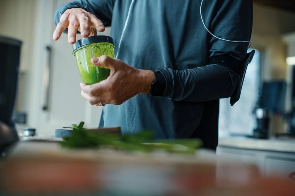 Adult male in athletic wear prepares a green smoothie in a modern kitchen, highlighting a healthy lifestyle with a focus on nutrition.