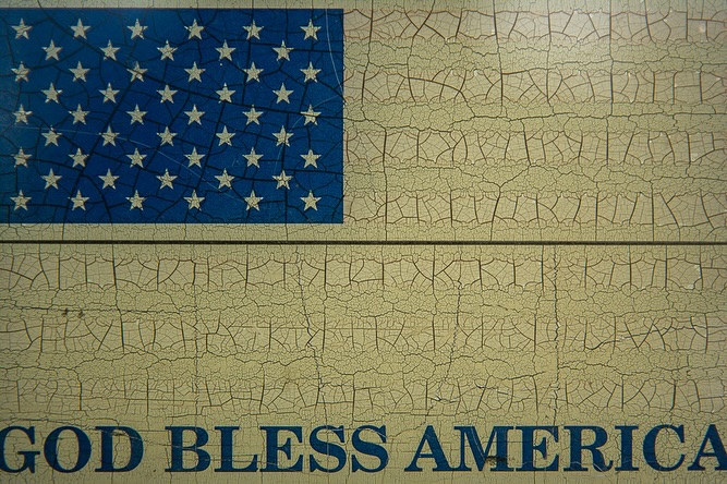 Distressed image of the American flag on wood paneling with the words 'GOD BLESS AMERICA' in blue lettering below.