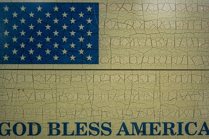 Distressed image of the American flag on wood paneling with the words 'GOD BLESS AMERICA' in blue lettering below.