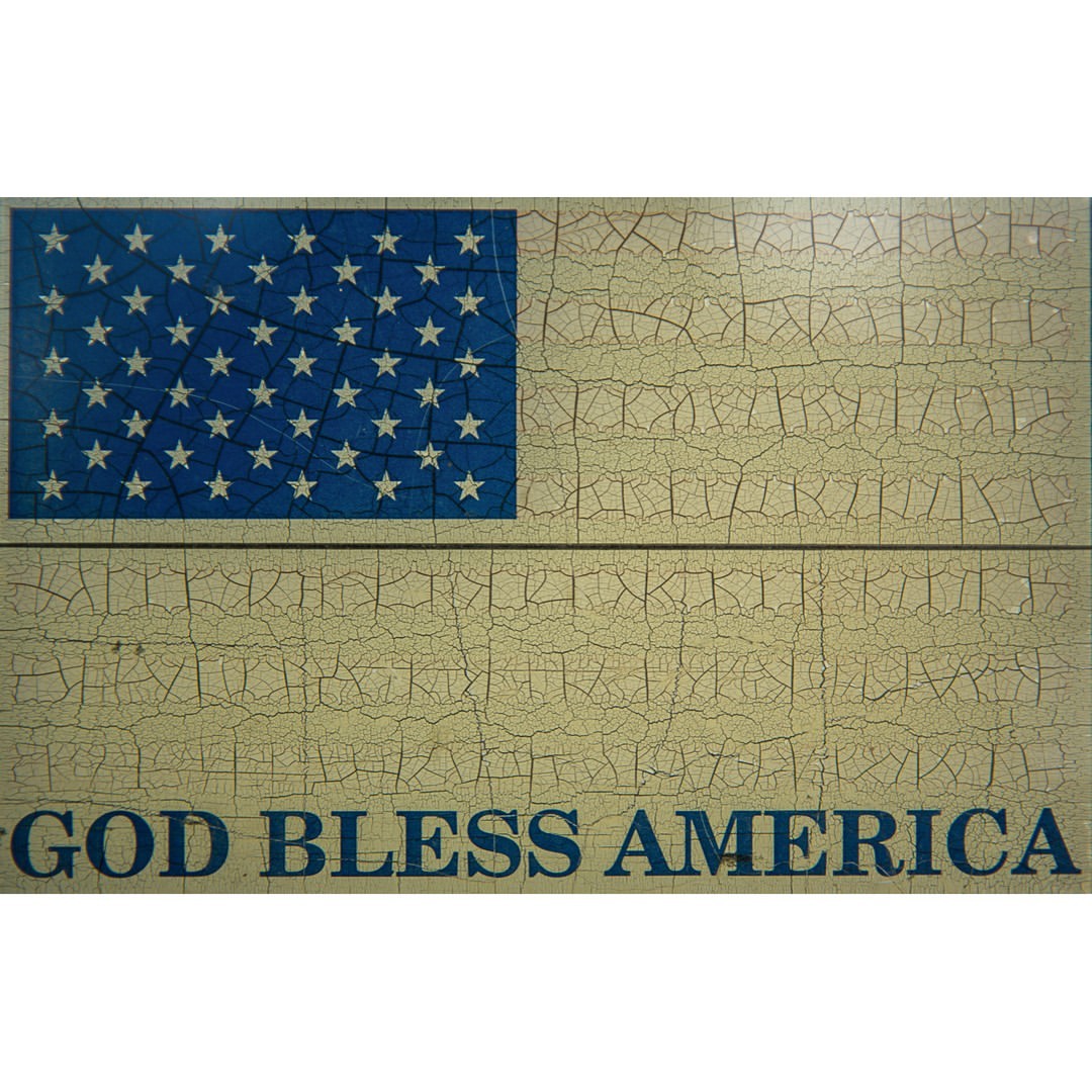 American flag graphic on a cracked, textured surface with 'God Bless America' text in blue, creating a patriotic and aged aesthetic.