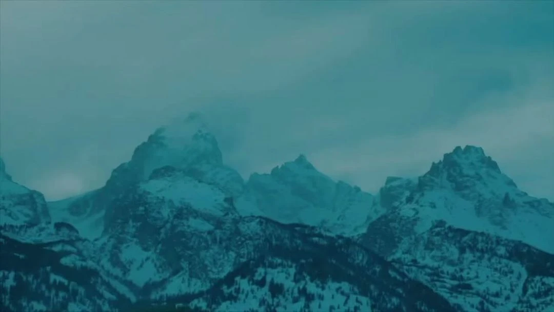 Snow-capped mountains under an overcast sky create a cool, atmospheric landscape scene with visible peaks and valleys.