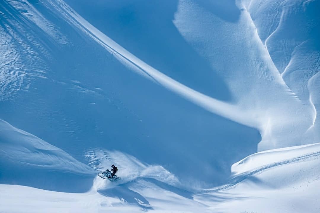 Snowmobile rider ascends a snowdrift in an outdoor mountain environment, showcasing a winter adventure and blue color grading.
