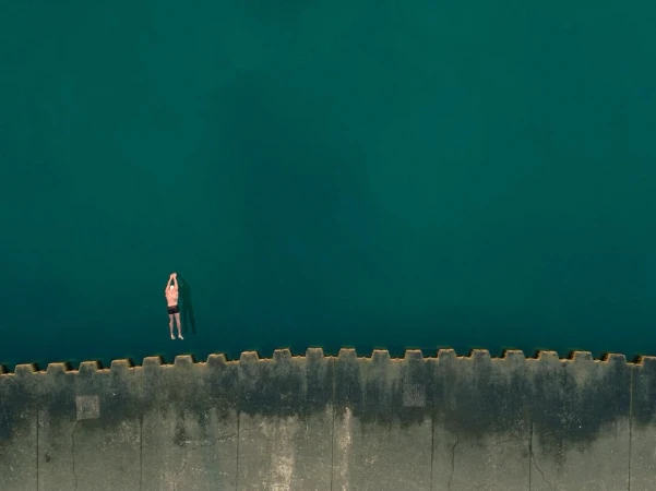 Aerial view of an adult male floating in turquoise water next to a concrete pier on a sunny day, showing tranquility and open water.
