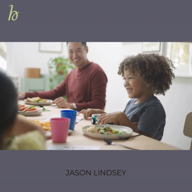 A family gathers around a table for a meal, featuring a smiling child and father, with dishes and drinks in a brightly lit interior.