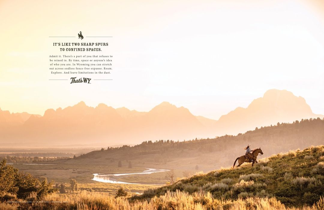 Landscape shot of a person riding a horse on a grassy hill with a mountain range visible in the background during golden hour.