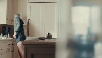 Man in a kitchen wearing a pajama top and shorts gets coffee by the kitchen counter. There are white cabinets in the background.