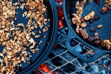 Cast iron skillets filled with toasted oats and nuts roasting over an open fire grill grate