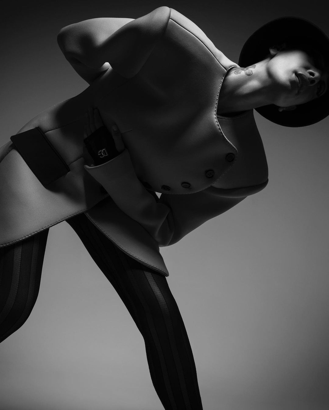 Fashionable woman in black hat and jacket strikes a pose in studio lighting. Black and white portrait highlights her stylish attire.
