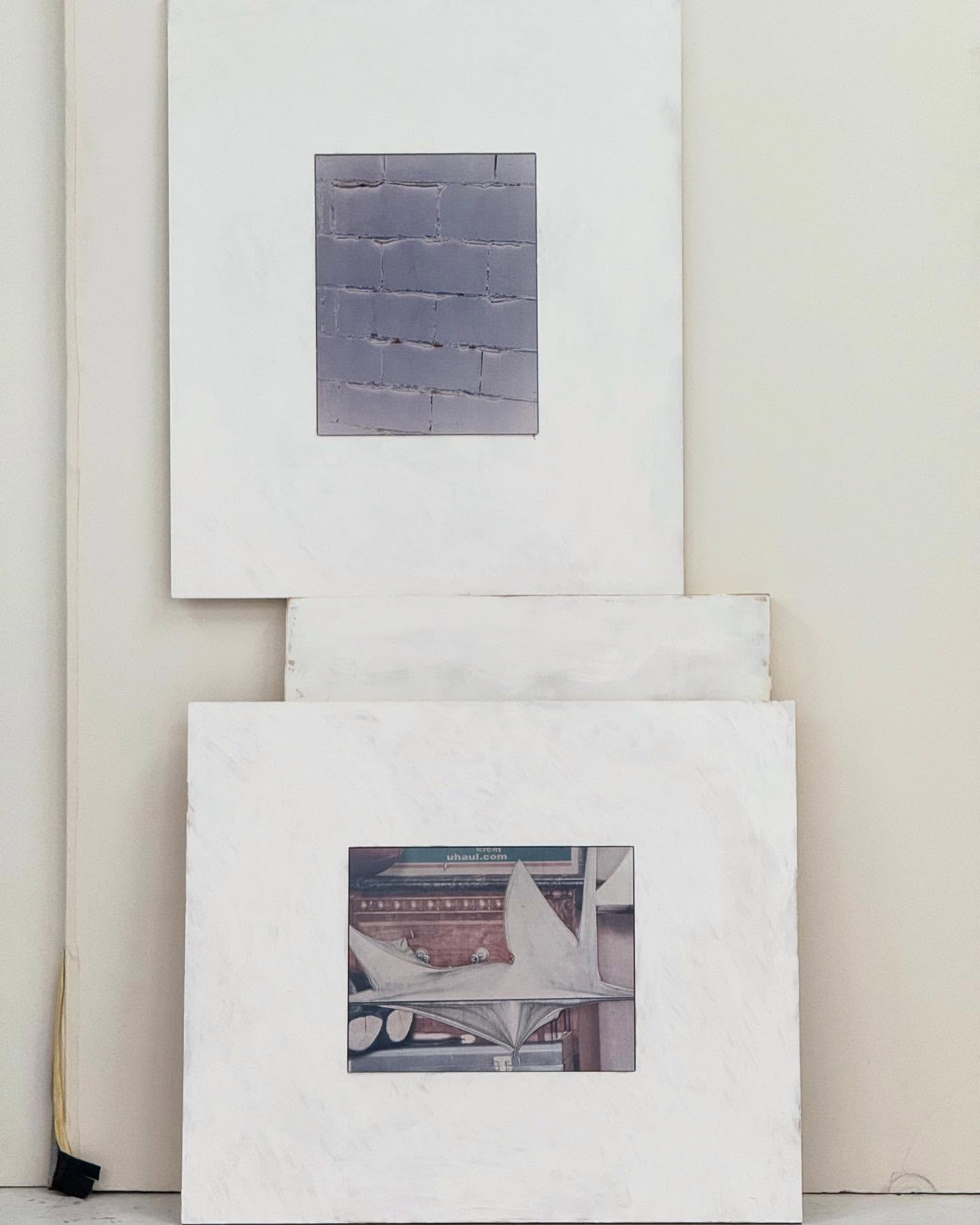 Two framed artworks hang on a white wall. The first artwork is a brick wall and the second artwork is of a white statue.
