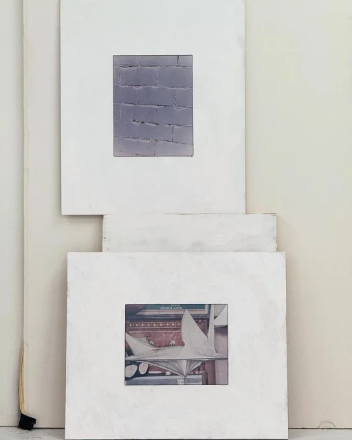 Two framed artworks hang on a white wall. The first artwork is a brick wall and the second artwork is of a white statue.