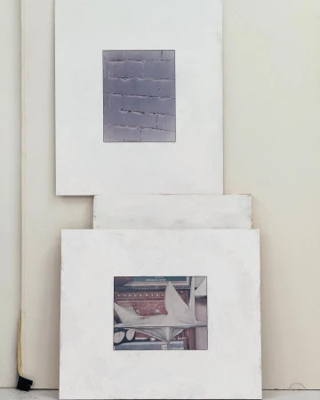 Two framed artworks hang on a white wall. The first artwork is a brick wall and the second artwork is of a white statue.