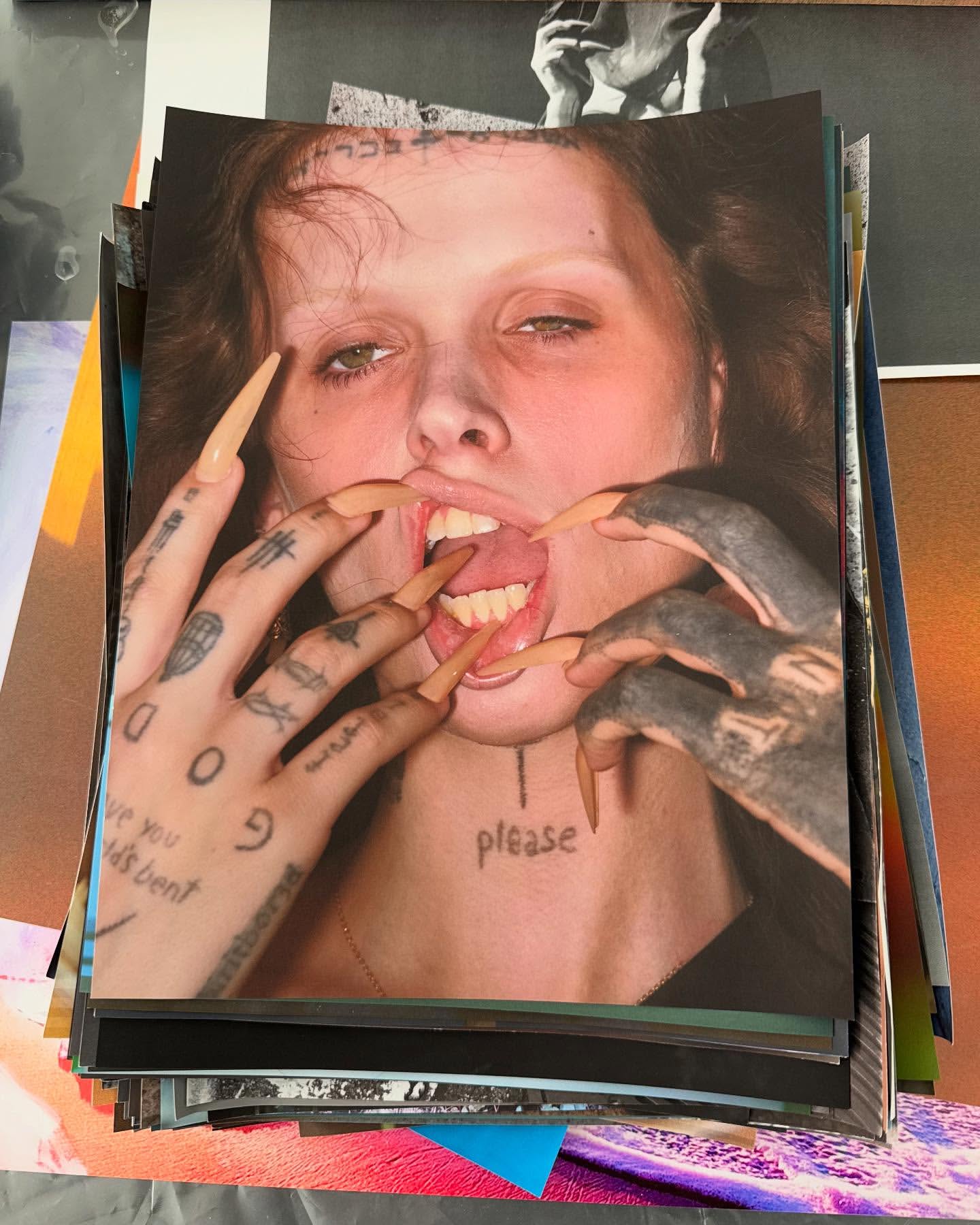 Close-up photo of a woman with long nails, tattoos, and the word 'please' tattooed on her neck, stacked in a pile of photos.