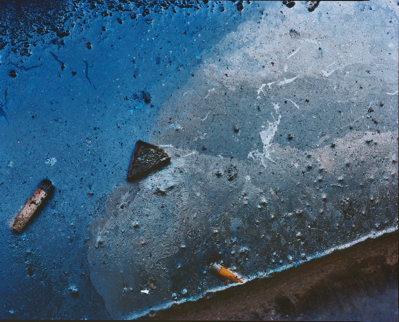 Textured abstract macro shot of dark blue liquid substance with fragments and light gray marble effect, creating an artistic background.